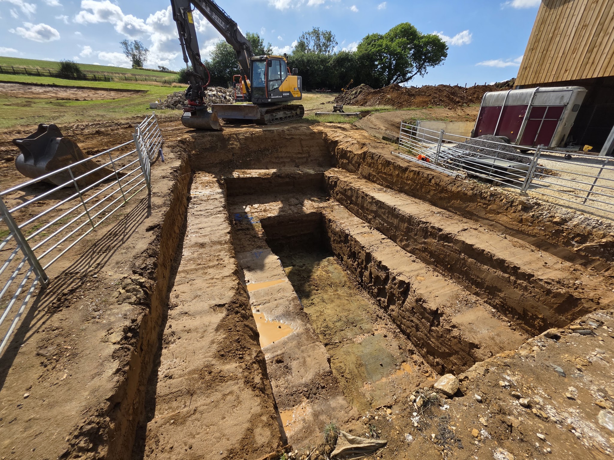Deep stepped excavation beside a timber barn