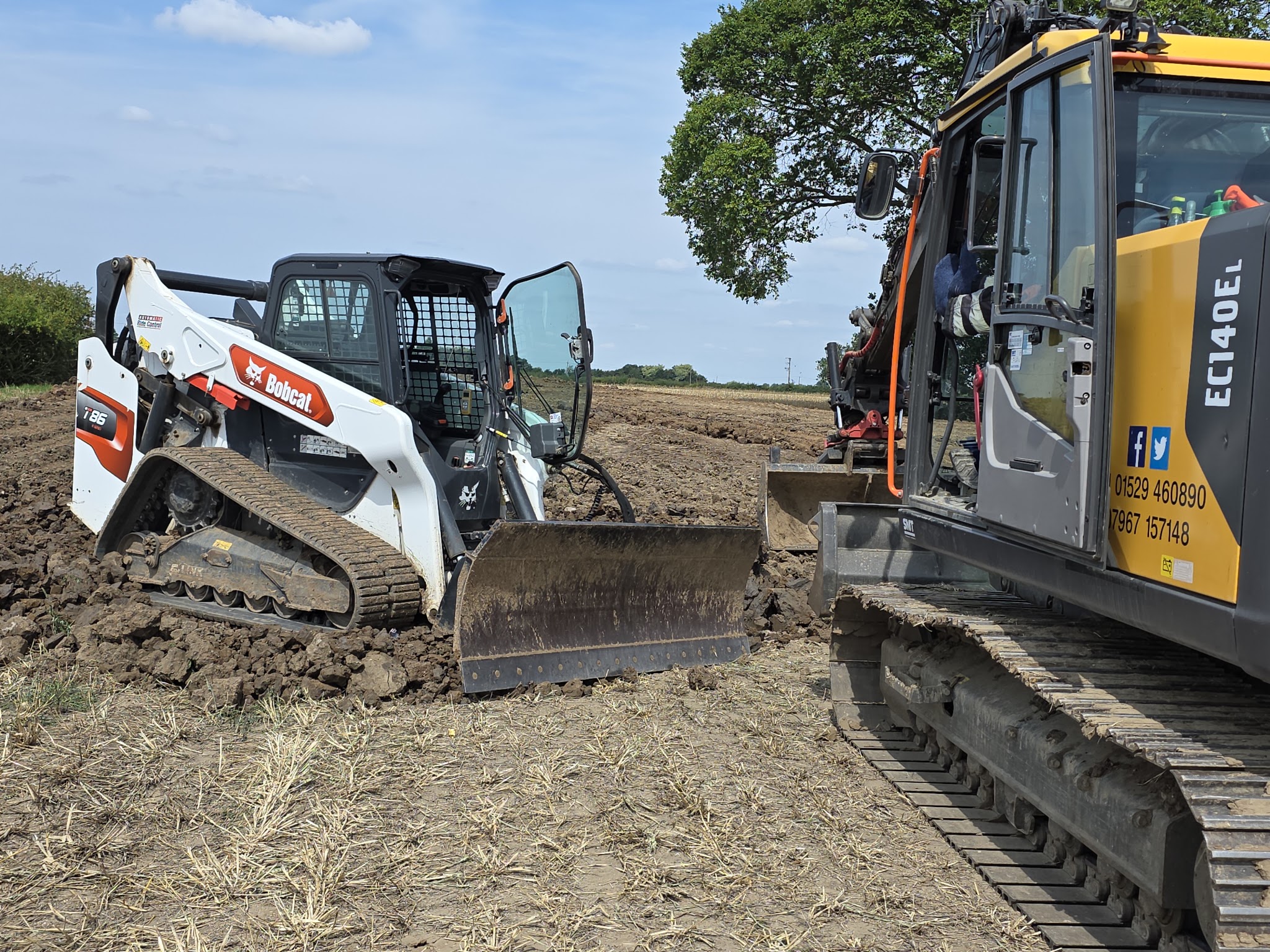 Tracked loader and S.E. Hill Volvo excavator on a cleared field
