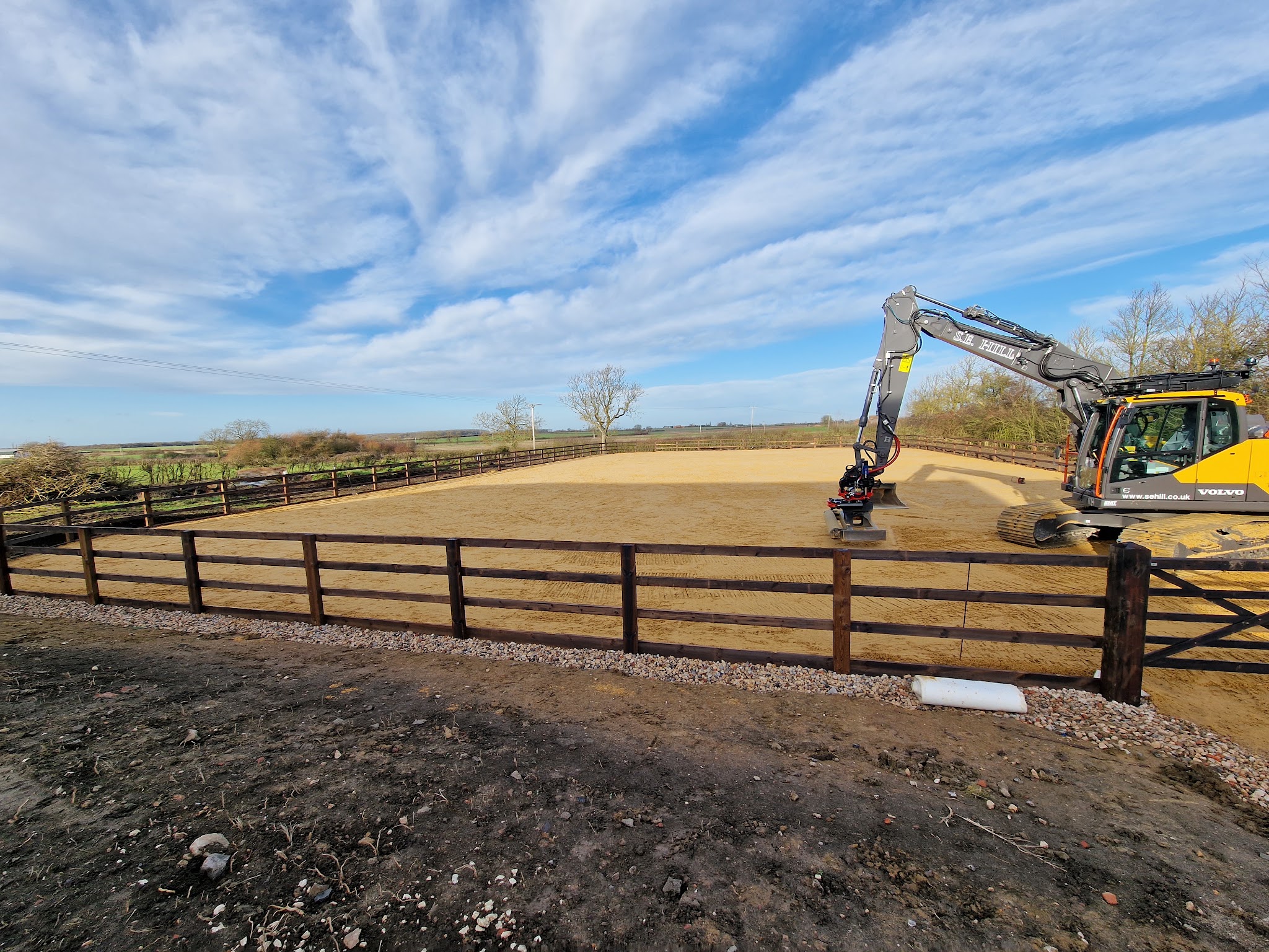 A finished S E Hill arena with dark post and rail fencing and the firm's Volvo excavator