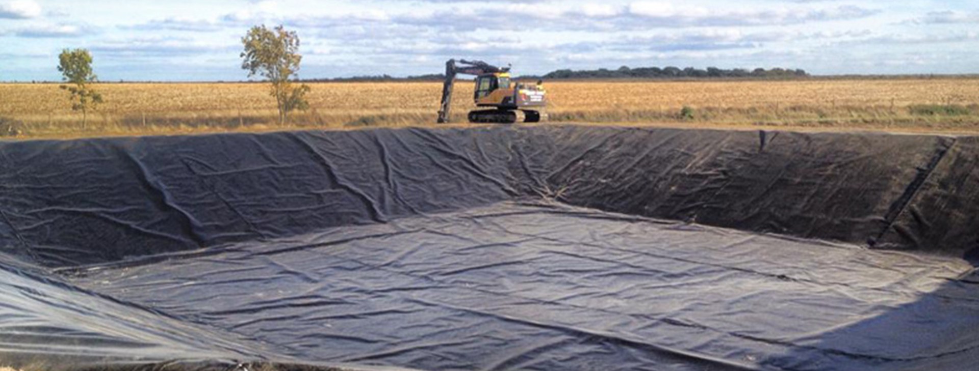 Large lined reservoir with an excavator working on the far bank