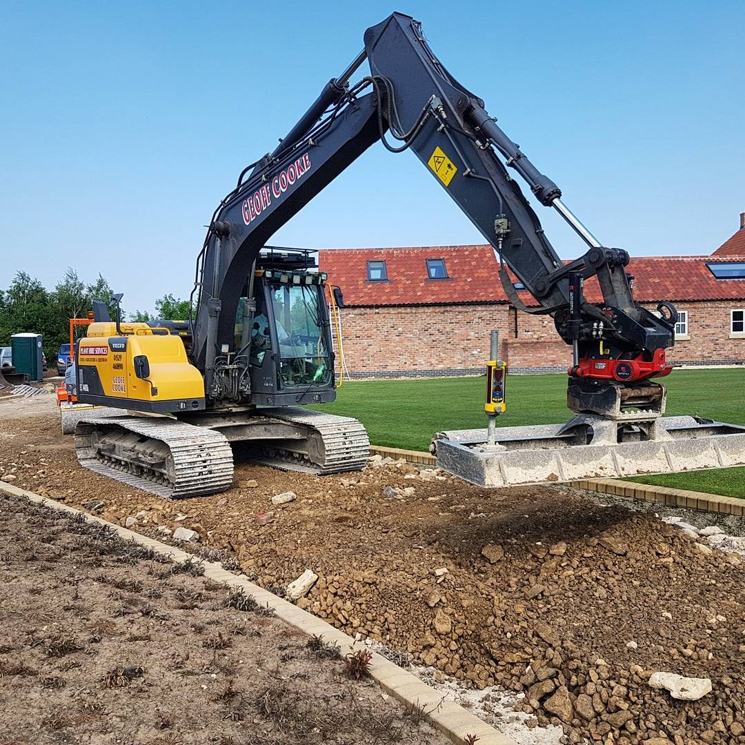 Excavator with roller attachment at a farmhouse