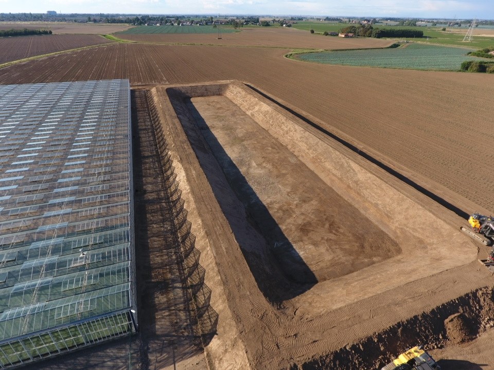 Aerial view of a reservoir under construction next to glasshouses