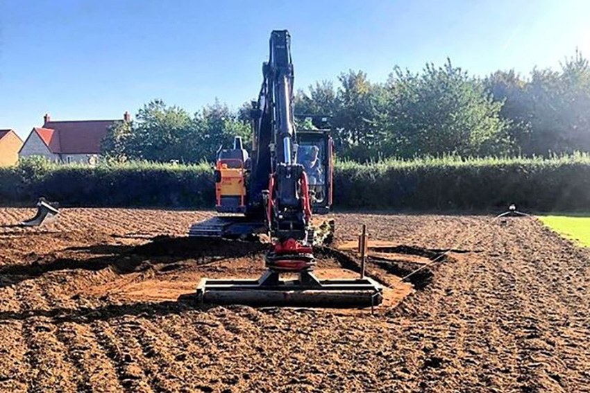 Excavator levelling a plot beside new houses