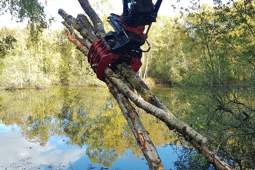 Grapple lifting cut timber beside a pond