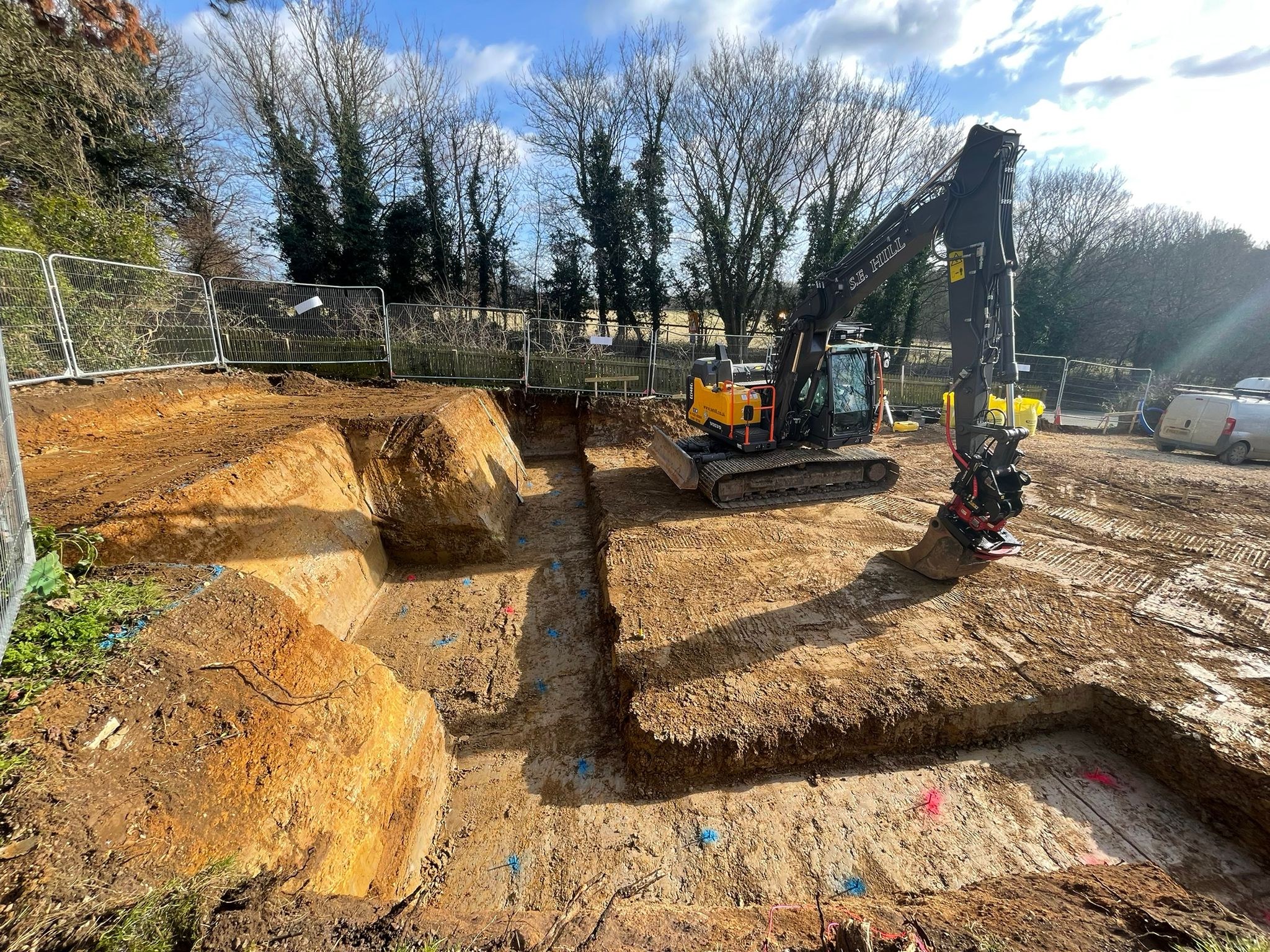 Excavator working a deep foundation dig behind site fencing